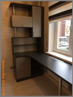 an empty desk in the corner of a room with a large window and some cabinets