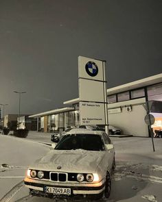 a white car parked in front of a bmw dealership on a snowy street at night