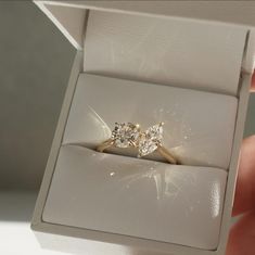 someone is holding an engagement ring with three diamonds on it in a white gift box