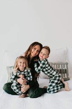 a woman and two children sitting on top of a bed in matching green plaid pajamas