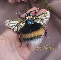 a hand holding a small insect with pearls on it's body and wings,