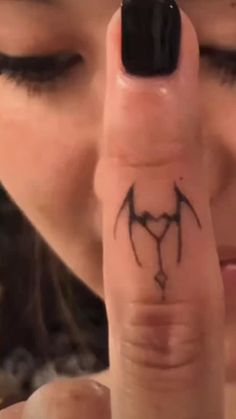 a woman is holding her finger up to the camera with a bat tattoo on it