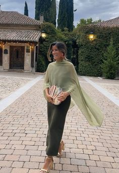 a woman standing in front of a building holding a purse and smiling at the camera