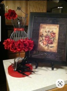 there are roses on the counter next to an old framed painting and wire vase with flowers in it