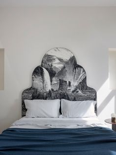 a bed with white sheets and blue blankets in a room that has a painting on the headboard