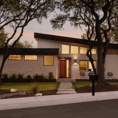 a house with trees and grass in front of it at dusk, lit up by street lights