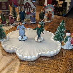 a group of figurines sitting on top of a wooden table next to christmas trees