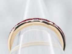 This is such an easy ring to wear! It sits low to the hand, and the sparkling synthetic ruby gemstones are set flush to the metal - there are no prongs to snag on this band! Crafted of 14-karat yellow gold, the flat sides will sit snug against an engagement ring, and stack with other bands with no gaps. *Please note, that one of the rubies is chipped and this piece has been priced accordingly.Metal: 14K Yellow GoldGem: Synthetic RubiesWidth of Band: 2.6 mmHeight off Finger: 2.1 mmRing Size: 5.50Marks: "14K" Stamped on the inside band Yellow Gold Ruby Round Cut Eternity Band, Modern Yellow Gold Ruby Ring For Wedding, Gold Ruby Ring With Brilliant Cut, Gold Ruby Half Eternity Round Cut Ring, Gold Ruby Ring Half Eternity Style, Yellow Gold Ruby Ring With Polished Finish, Gold Ruby Ring With Half Eternity Design, Yellow Gold Ruby Half Eternity Ring, Yellow Gold Ruby Ring With Channel Setting For Anniversary