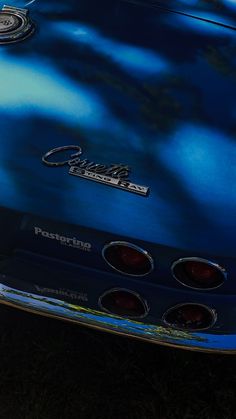 the front end of a blue classic car parked on grass with trees in the background