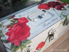 a painted box sitting on top of a wooden floor next to a window with red flowers