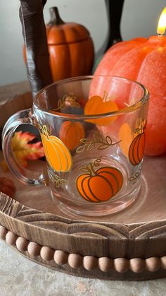 a glass cup sitting on top of a wooden tray with pumpkins in the background