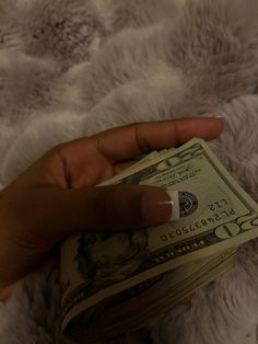 a person's hand holding money on top of a white fur covered bed spread