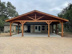 a covered parking lot in front of a stone building with wood beams on the roof