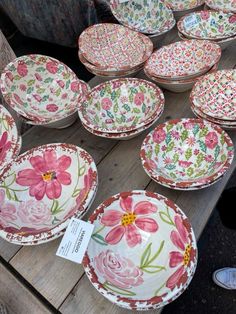 many plates with flowers on them sitting on a wooden table in front of other dishes