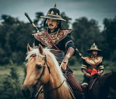 two men dressed in period costumes riding on horses with spears sticking out of their mouths