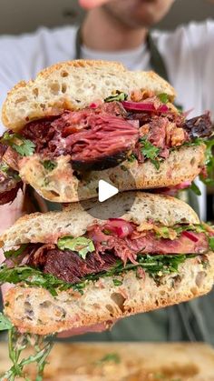 a man is holding two sandwiches with meat and greens on them in front of him