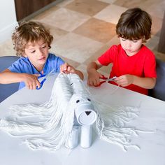 two young boys are working on a paper dog sculpture at a table in the living room