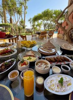 a table filled with lots of food on top of a glass topped table next to palm trees