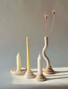 three candles and two vases with flowers in them sitting on a table top next to each other