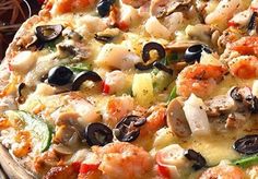 a pizza with shrimp, olives, and mushrooms on it sitting on a table