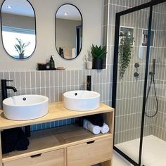 two white sinks sitting on top of a wooden cabinet in a bathroom next to a walk in shower