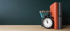 an alarm clock sitting on top of a wooden table next to books and pencils