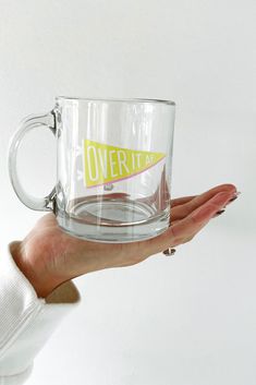 a person holding a clear coffee mug with an over it sticker on the side