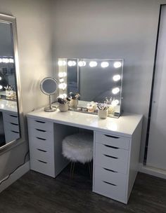 a white vanity with lighted mirrors and stool