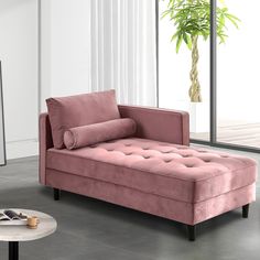 a pink couch sitting in front of a window next to a table with a potted plant on it