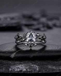 a white diamond ring sitting on top of a black rock with other rocks in the background