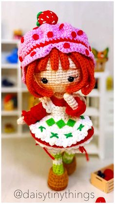 a small doll is wearing a knitted hat and holding a crochet dress