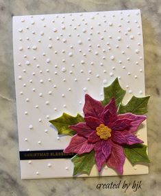 a christmas card with poinsettia leaves and dots on the paper, sitting on a marble surface