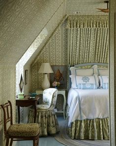 a bed sitting under a window next to a chair and table in a room with white walls