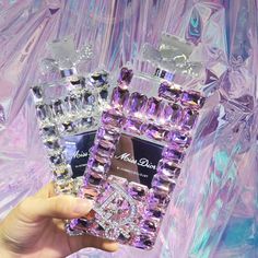 a person holding up two perfume bottles in front of purple and blue ice crystals background