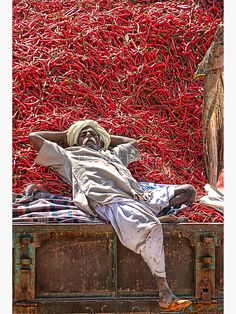 a man laying on top of a crate next to a pile of red chili peppers