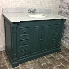 a bathroom vanity with white marble top and dark green cabinetry, against a brick wall