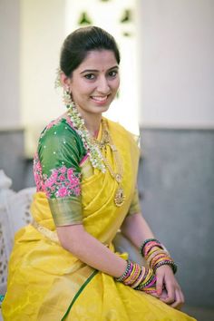 a woman in a yellow and green sari sitting on a white bench with jewelry