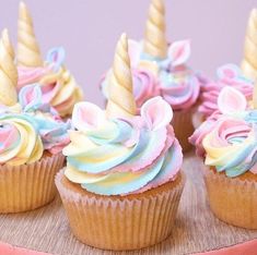 cupcakes decorated with pastel icing and unicorn horn decorations on a wooden tray