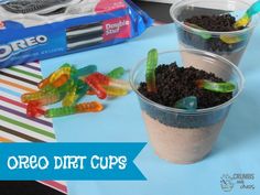 two cups filled with dirt and gummy bears sitting on top of a blue table