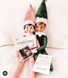 two elfs are sitting on a bed next to each other and one is holding a calendar