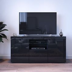 a black entertainment center with a large television on it's stand in front of a potted plant