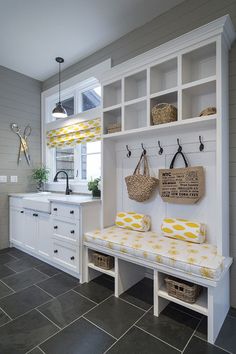 a kitchen with white cabinets and yellow cushions on the bench in front of the sink