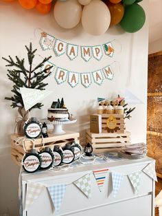 a dessert table with balloons, cake and decorations on the wall behind it for a camp birthday party