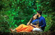 a man and woman sitting next to each other on the ground in front of trees