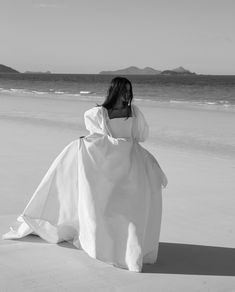 a woman in a white dress sitting on the beach