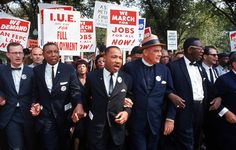 a group of men in suits and ties standing next to each other with protest signs behind them