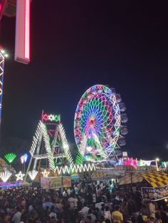 an amusement park at night with ferris wheel and carnival rides in the background as well as many people standing around