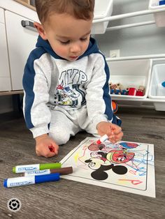 a little boy sitting on the floor playing with some crayons and coloring paper