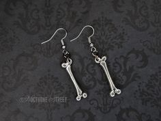 A beautiful pair of gothic dangle earrings designed by Nocturne Street, featuring Tibetan Silver femur bone charms hanging from Silver Plated hooks. The earrings will be packaged in a pretty organza gift bag and would make a lovely gift. The drop length is approximately 35mm and the bones are approximately 10mm wide at their widest point. Visit my shop to see the complete collection of gothic earrings. Only pay one lot of postage, the rest of your order ships free! Creepy Earrings, Femur Bone, Earrings Gothic, Goth Necklace, Goth Earrings, Bone Earrings, Gothic Earrings, Halloween Earrings, Organza Gift Bags