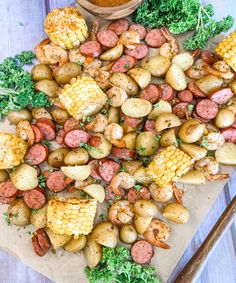 a platter filled with potatoes, corn and sausage next to a bowl of broccoli